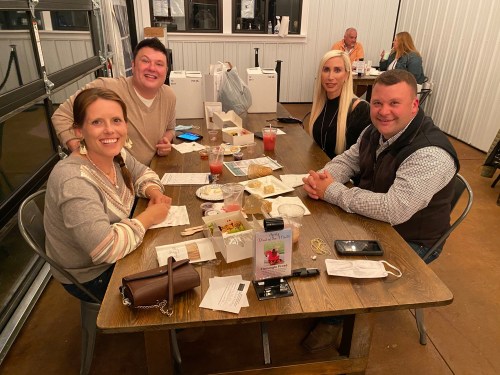 A group of four people sitting at a table with food and drinks, smiling and enjoying their time together.