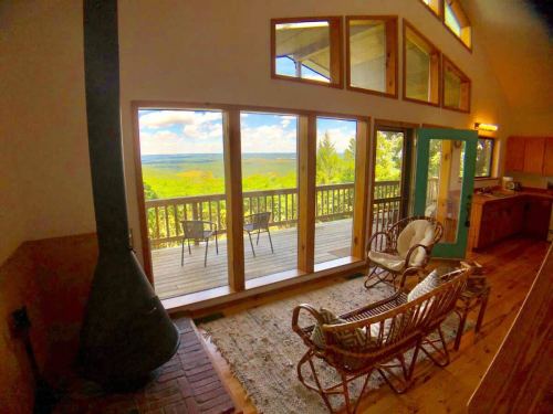 Cozy interior with two chairs, a wood stove, and large windows showcasing a scenic view of nature outside.