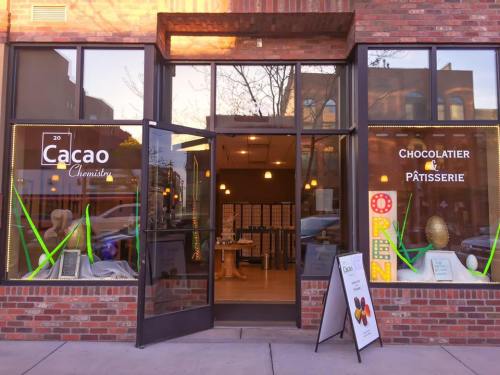 Exterior of a chocolate shop with large windows, displaying "Cacao Chemist" and "OPEN" signs, and a welcoming entrance.