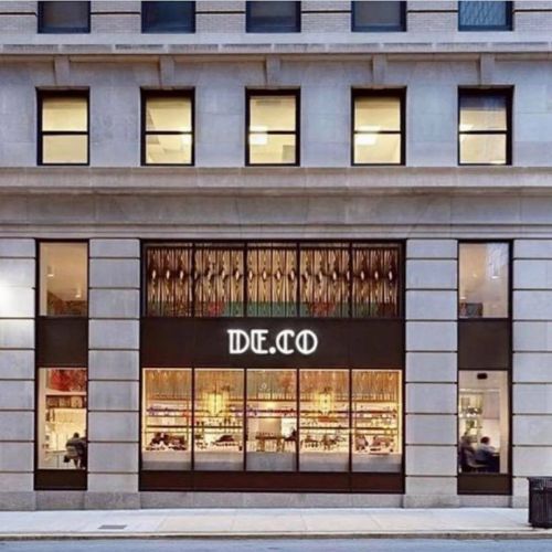 A modern building facade featuring large windows and a stylish storefront with the name "DE.CO" prominently displayed.