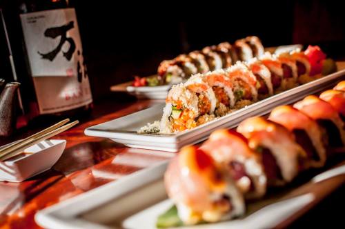 A variety of colorful sushi rolls arranged on white plates, with a bottle of sake in the background.