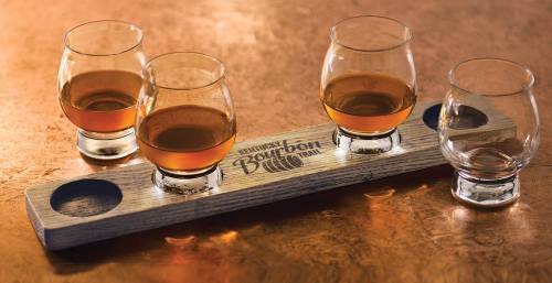 Four glasses of bourbon on a wooden flight board, featuring the Kentucky Bourbon Trail logo.