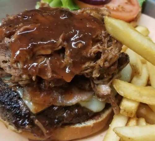 A hearty burger topped with pulled pork and barbecue sauce, served with fries and fresh lettuce and tomato.