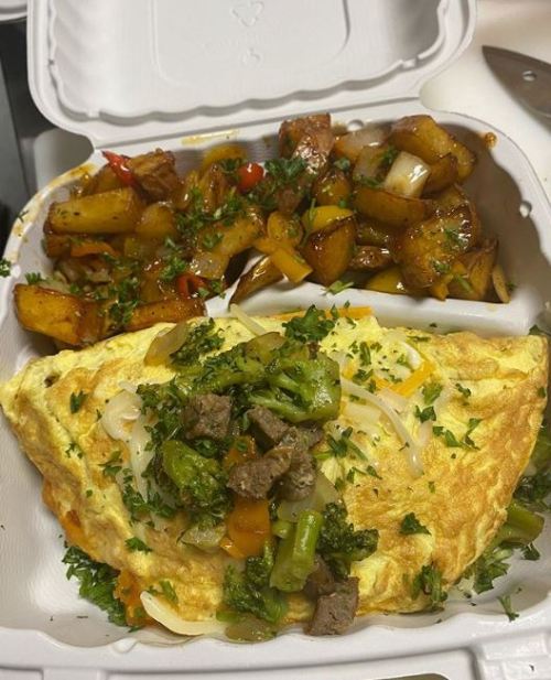 A hearty omelette topped with vegetables and beef, served with seasoned roasted potatoes on the side.