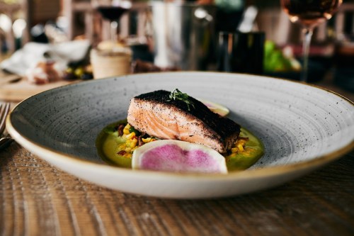 A beautifully plated dish featuring a seared salmon fillet on a bed of vibrant puree, garnished with radish slices.