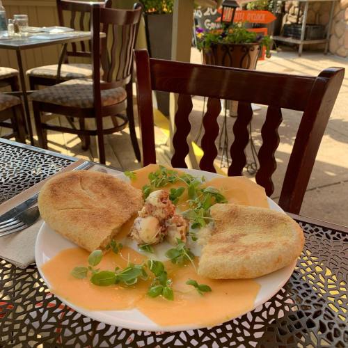 A plate with two halved pancakes, drizzled with sauce and garnished with microgreens, on a table outdoors.