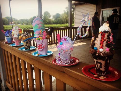 A colorful display of extravagant ice cream sundaes topped with various candies and decorations on a wooden table.