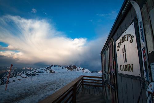 A wooden cabin sign reading "Corbet's Cabin" with snowy mountains and dramatic clouds in the background.