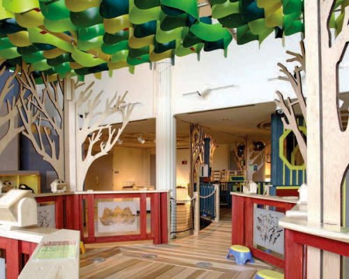 A colorful indoor play area with tree-like structures and green ceiling decorations, inviting exploration and creativity.