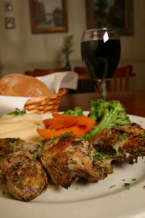 A plate of seasoned chicken thighs with broccoli, carrots, and bread, accompanied by a glass of red wine.