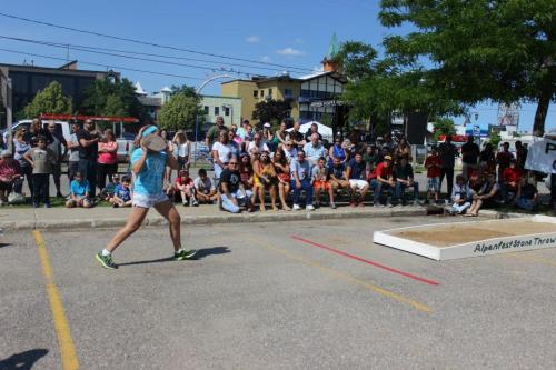 A competitor throws a stone in a stone-throwing event, with a crowd watching in the background on a sunny day.