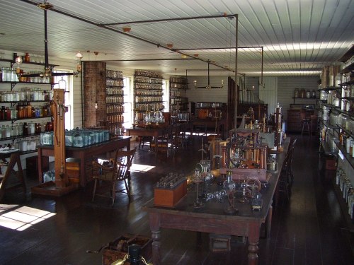A vintage laboratory filled with glass bottles, wooden tables, and scientific equipment, illuminated by natural light.
