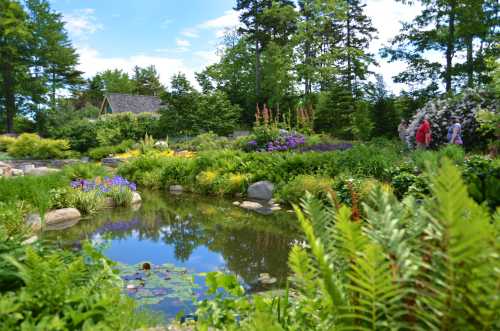 A lush garden with colorful flowers, a pond, and two people walking along a path surrounded by greenery.