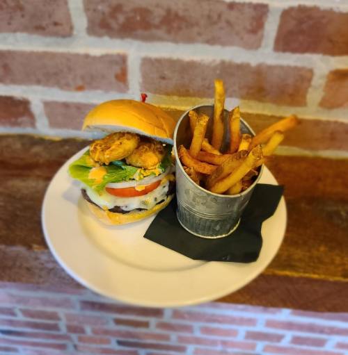 A delicious burger with lettuce, tomato, and a pickle, served with a side of crispy fries in a metal cup.