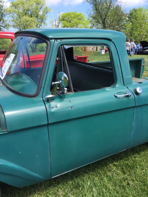 A vintage green pickup truck parked on grass, showcasing its classic design and shiny side mirror.