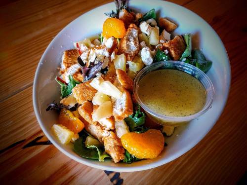 A colorful salad with greens, chicken, mandarin oranges, pineapple, and croutons, served with a dressing on the side.