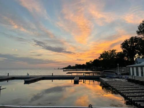 Sunset over a calm lake, with colorful clouds reflecting on the water and docks in the foreground.