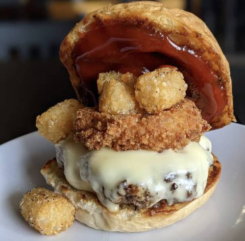 A hearty sandwich with a fried chicken patty, melted cheese, tater tots, and a sweet sauce on a toasted bun.