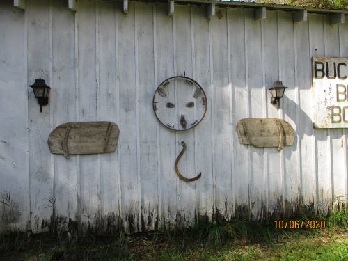 A weathered white wall with two wooden sleds, a circular face-like design, and a horseshoe, surrounded by grass.