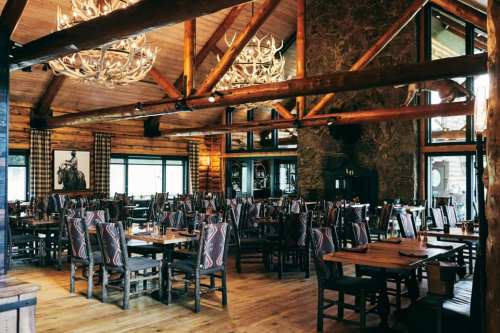 Cozy restaurant interior with wooden beams, rustic decor, and multiple tables surrounded by patterned chairs.