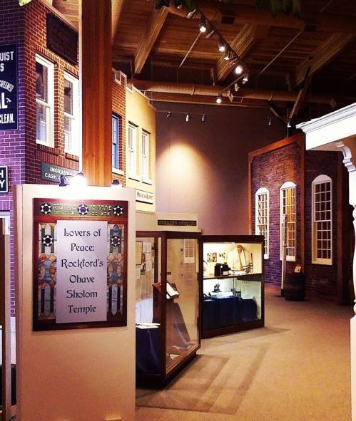 Interior of a museum featuring displays about Rockford's Ohave Sholom Temple, with brick walls and glass cases.