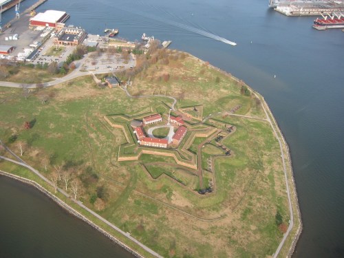 Aerial view of a star-shaped fort surrounded by water, with green grass and buildings inside the fort.