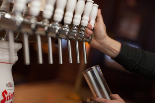 A hand reaches for a beer tap, preparing to fill a glass from a row of shiny draft beer faucets.