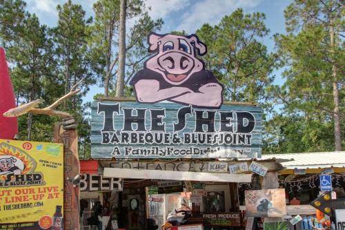 Sign for "The Shed Barbeque & Blue Joint" featuring a cartoon pig, surrounded by trees and colorful decorations.