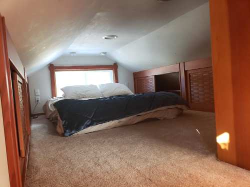 Cozy loft space with a bed, soft carpet, and natural light from a window.