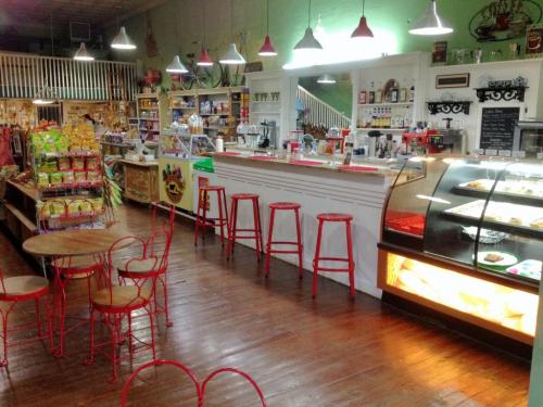 A cozy café interior with red chairs, a display case of pastries, and shelves stocked with snacks and drinks.