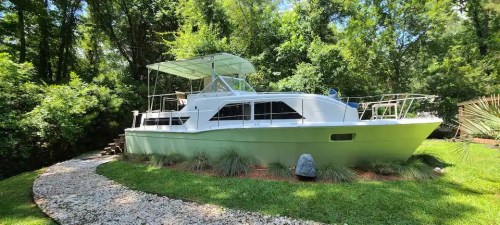 A white boat parked on a grassy area, surrounded by trees and a gravel pathway.