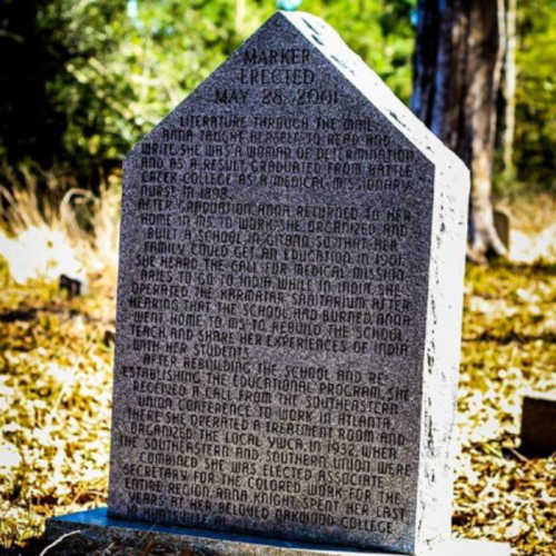 A stone marker commemorating a woman's contributions to education and missionary work, surrounded by trees.