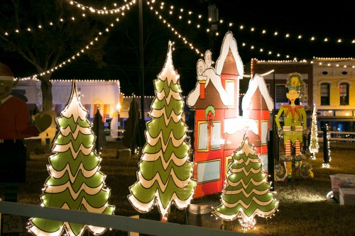 Colorful holiday decorations with illuminated trees, a bright house, and festive lights at night.