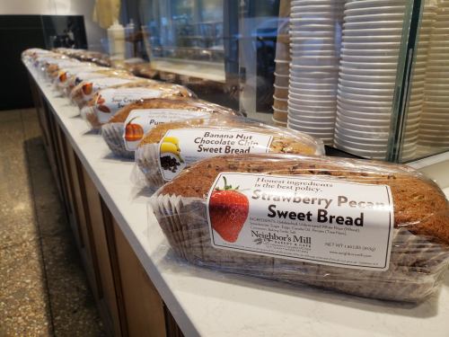A display of various sweet bread loaves, including strawberry pecan and banana nut, on a countertop.
