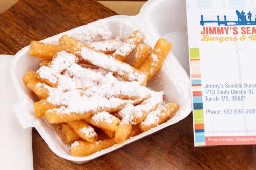 A takeout container filled with crispy fries dusted with powdered sugar, next to a restaurant business card.