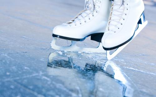 Close-up of white ice skates on a reflective ice surface, showcasing the blades and laces.