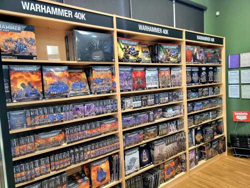 A display of Warhammer 40K products on shelves, featuring various game boxes and miniatures in a store setting.