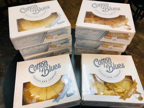 A stack of cheesecake boxes from Cotton Blues Cheesecake Company, featuring original and caramel flavors.