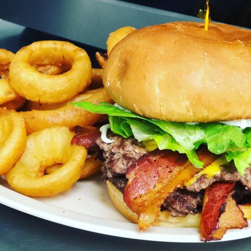 A juicy burger with lettuce, cheese, and bacon, served with a side of crispy onion rings on a white plate.