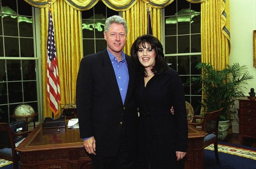 Bill Clinton and Monica Lewinsky pose together in the Oval Office, with the American flag and yellow curtains in the background.