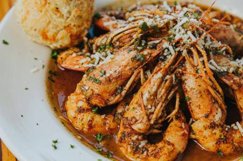 A plate of seasoned shrimp topped with herbs and cheese, served with a biscuit on the side.