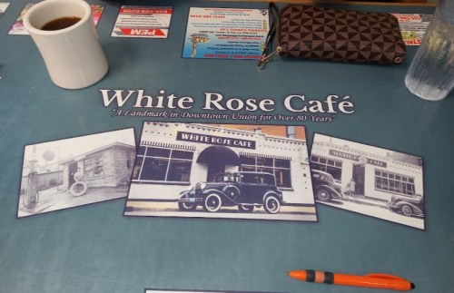 A table setting at White Rose Café featuring a coffee cup, a pen, and historical photos of the café.
