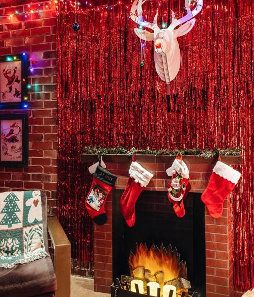 Cozy holiday scene with a decorated fireplace, stockings, and festive lights against a shimmering red backdrop.