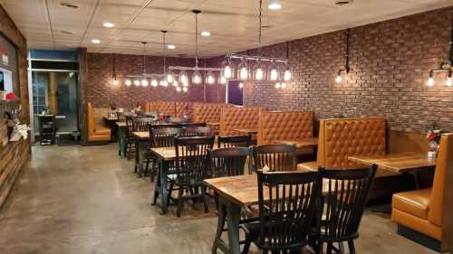 Cozy restaurant interior with wooden tables, black chairs, and warm lighting against a brick wall.