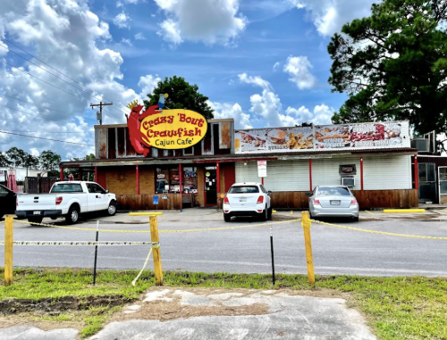 Exterior of Greggy B's Crawfish Cajun Cafe, featuring a colorful sign and parked cars under a partly cloudy sky.