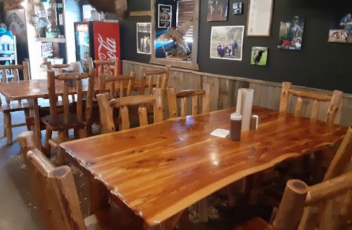 A rustic dining area with wooden tables and chairs, featuring photos on the walls and a soda machine in the corner.