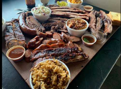 A large platter of assorted barbecue meats, sides, and sauces, including ribs, brisket, sausage, and rice.