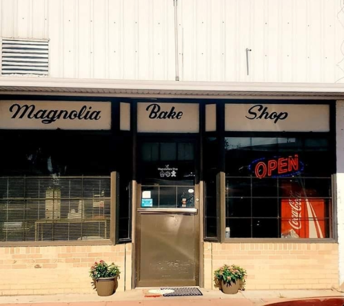 Front view of Magnolia Bake Shop with an "Open" sign and potted plants by the entrance.