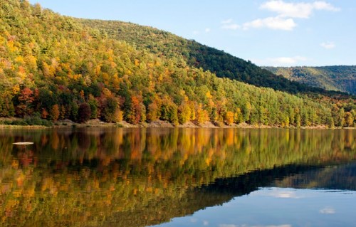 A serene lake reflecting colorful autumn trees and rolling hills under a clear blue sky.