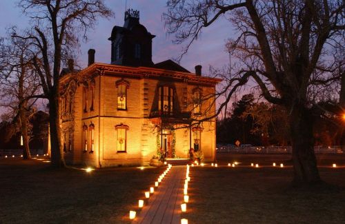 A historic house illuminated at dusk, surrounded by glowing lanterns along a pathway and bare trees.